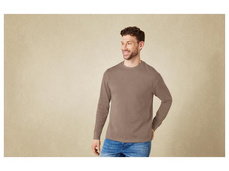 Man in een donkerbruin sweatshirt en blauwe jeans.