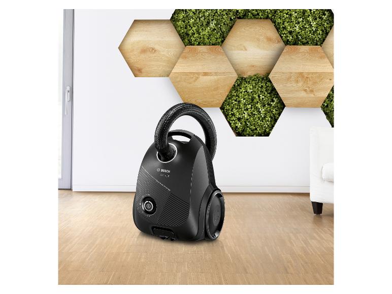 Zwarte stofzuiger op een houten vloer met een decoratieve wand van hout en planten.