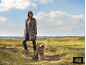 Vrouw in luipaardprint jas en bijpassende hond in een veld.