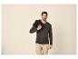 Man in donkergroen henley shirt en beige cargobroek, met een jas over zijn schouder.