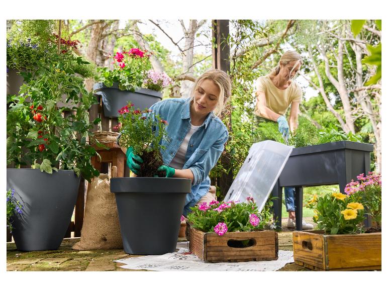 Twee vrouwen planten bloemen en groenten in potten en verhoogde plantenbakken in de tuin.