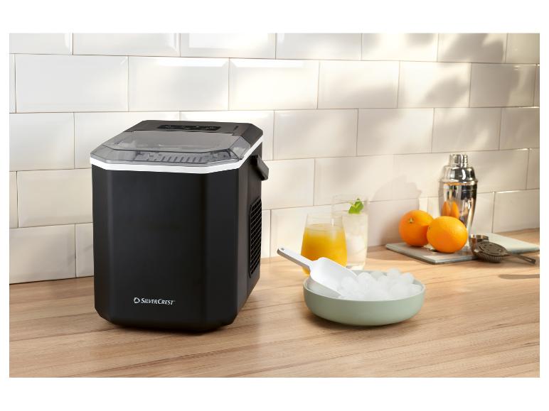 Zwarte ijsmachine met ijs, drankjes en cocktailshaker op een houten aanrecht.