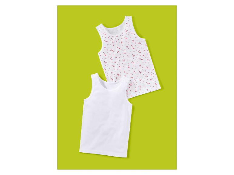 Twee witte kinderhemdjes, één effen en één met roze hartjesprint.