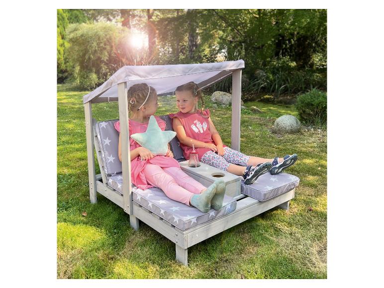 Twee kleine meisjes ontspannen op een houten tuinbank met kussens met sterrenpatroon.