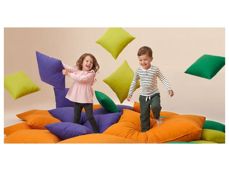 Twee lachende kinderen spelen met felgekleurde kussens.