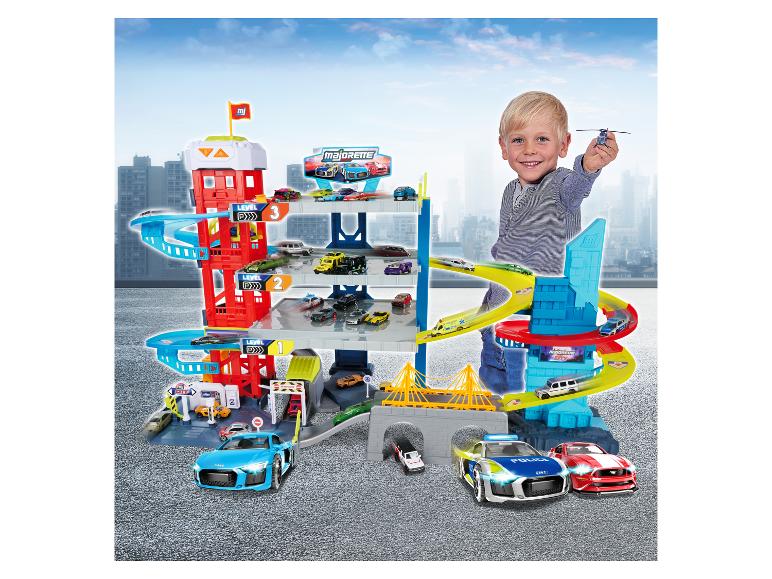 Jongen speelt met grote parkeergarage met meerdere verdiepingen, auto's en helikopter.
