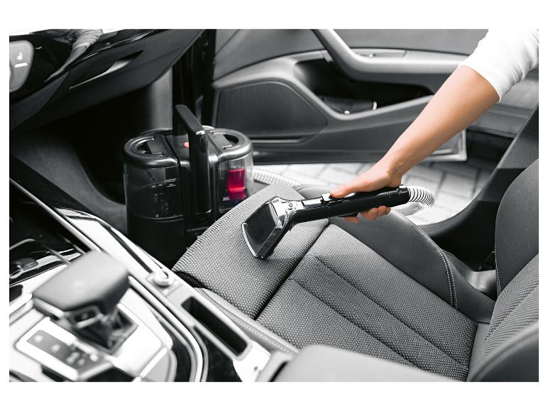 Handheld textielreiniger die een autostoel schoonmaakt.