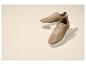 Twee bruine suède sneakers met witte zolen, één iets verhoogd op een wit blok.