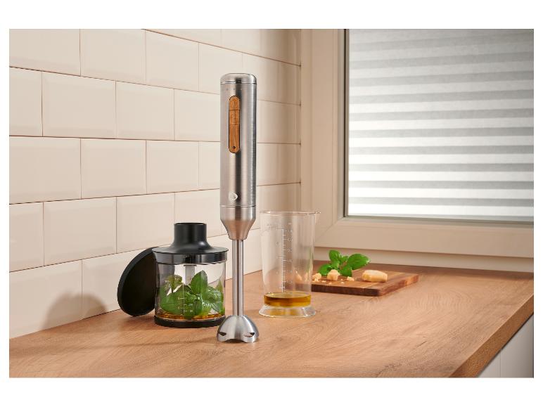 Roestvrijstalen staafmixer met houten accenten, die pesto bereidt op een houten aanrecht.