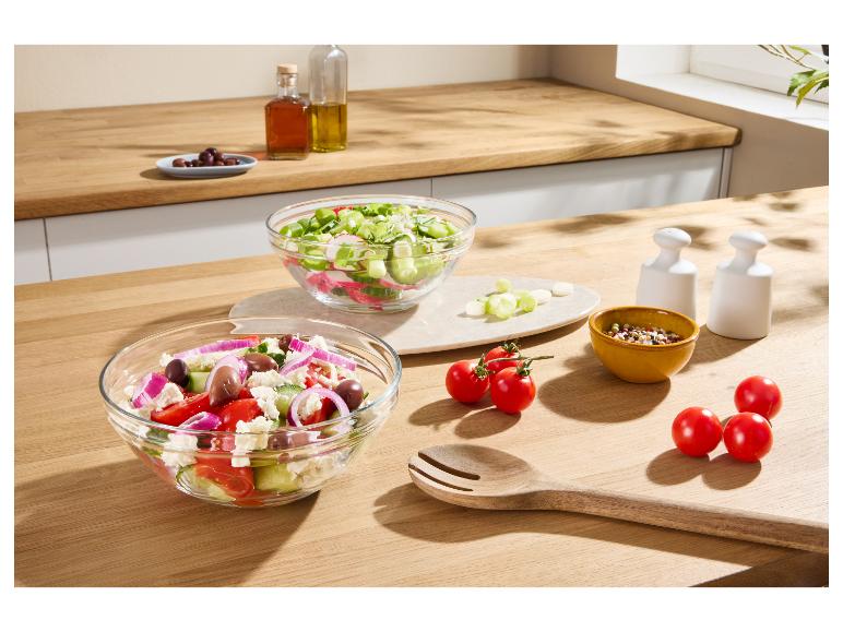 Verse salades in glazen kommen op een houten aanrecht met dressings en tomaten.