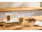 Twee glazen koffie latte, een leeg glas, macarons en bruine suiker op een houten tafel.