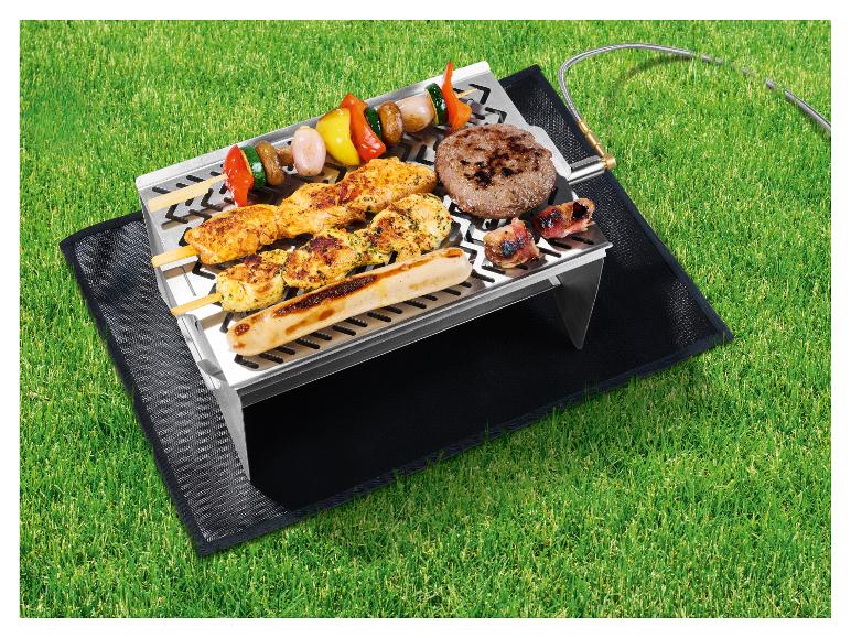 Gasbarbecue met spiesjes, burger en worst op gras.