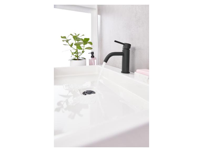 Een zwarte kraan in een moderne badkamer met een wastafel en water dat erin stroomt.