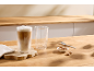 Twee latte macchiato glazen, één vol en één leeg, met koekjes en een lepeltje.