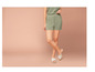 Vrouw draagt groene shorts en witte sandalen.