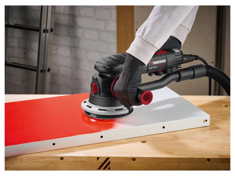 Handschuurmachine schuurt een rood oppervlak op een houten tafel.