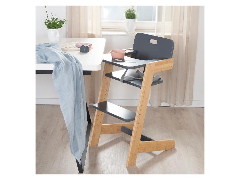 Houten en grijze kinderstoel met roze kom en lepel, naast een witte tafel.