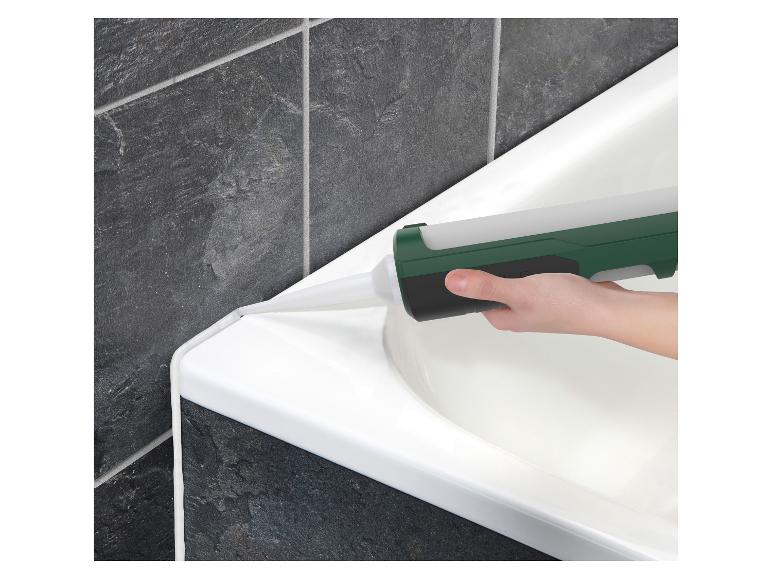 Hand brengt kit aan op de rand van een wit bad tegen donkergrijze tegels