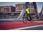 Man in geel fietsjack en zwarte helm op een elektrische fiets op een brug.