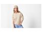 Vrouw in beige muts, beige trui en blauwe jeans.