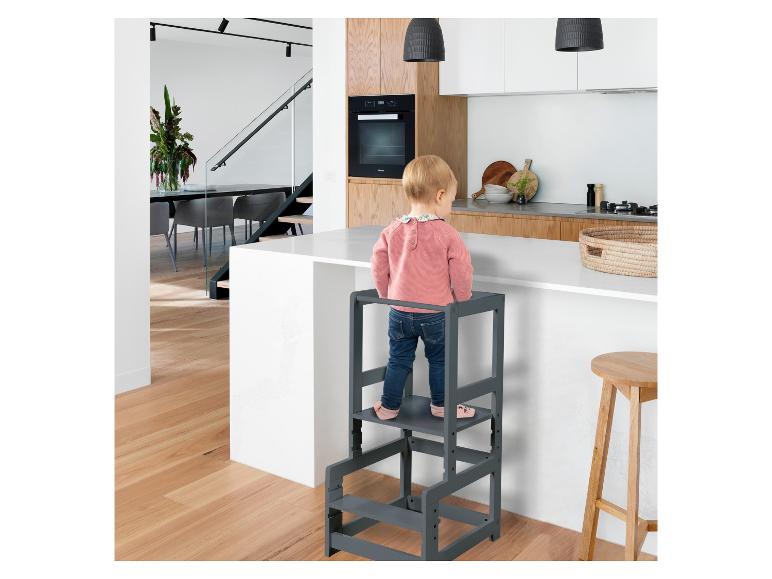 Kind op leertoren in moderne keuken met houten vloeren en wit eiland.