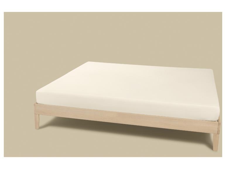 Licht houten bedframe met witte matras op een beige achtergrond.