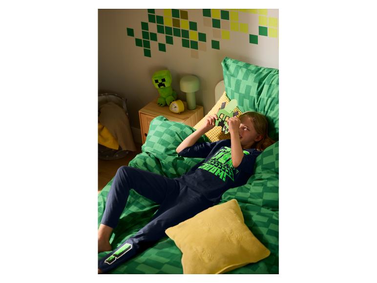 Kind in Minecraft-pyjama, liggend op bed met bijpassend beddengoed en themadecoratie.