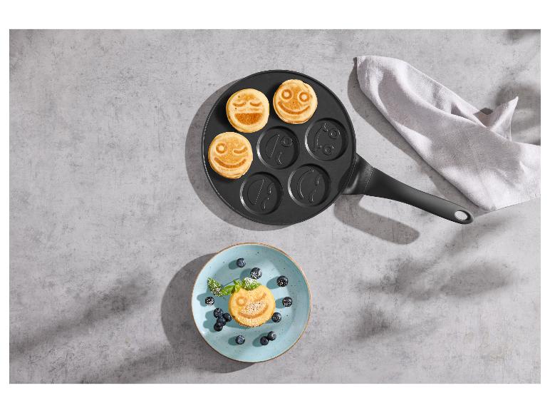 Pannenkoekenpan met smileys en bord met pannenkoek en bosbessen op betonnen achtergrond.