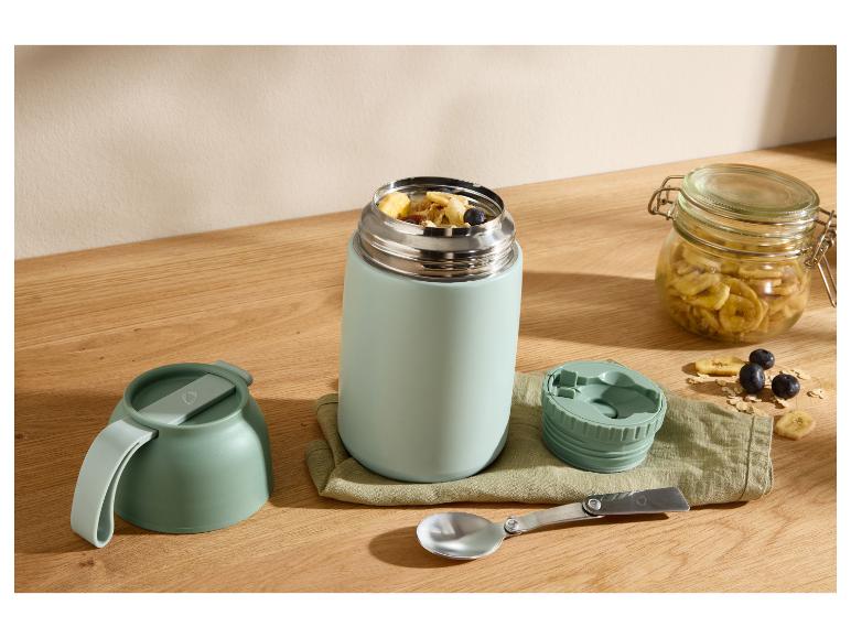 Voedselthermoskan met ontbijt, kom, lepel en pot gedroogde bananen op een houten tafel.