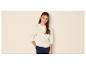 Meisje in beige sweatshirt en donkerblauwe broek, met hand in zak.