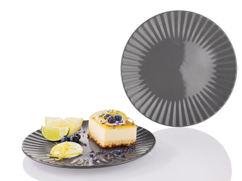 Een grijs bord met een stuk citroen cheesecake en partjes limoen.