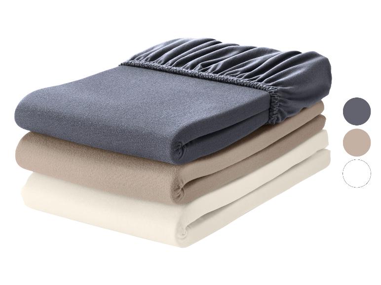 Stapel van drie gekleurde hoeslakens: donkergrijs, beige en crème.