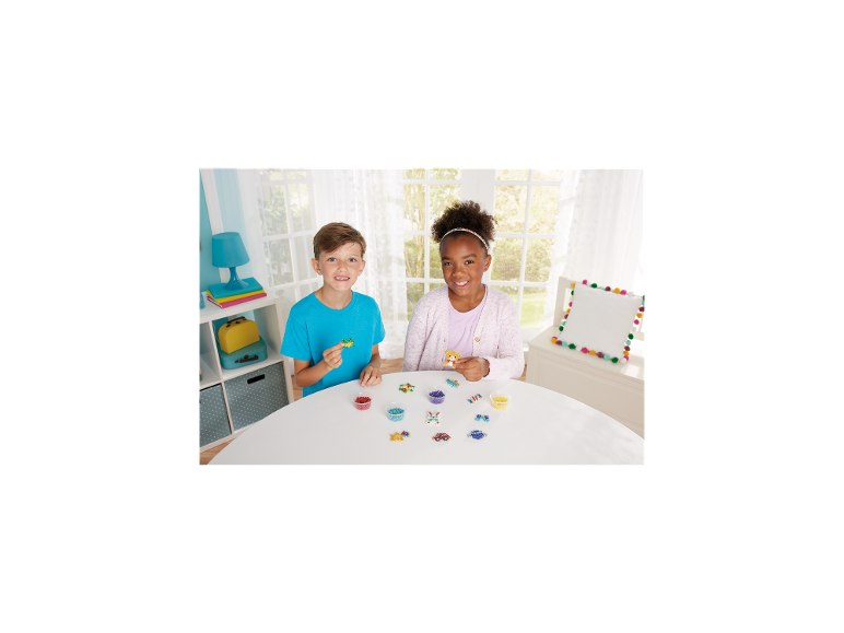 Twee kinderen spelen met strijkkralen en maken kleurrijke vormen op een witte tafel.