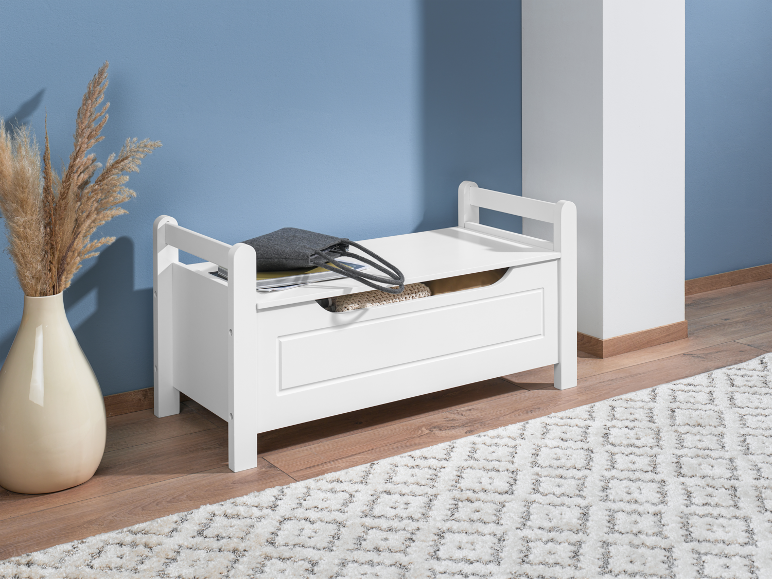 Wit houten opbergbankje met scharnierend deksel op een kleed in een kamer.