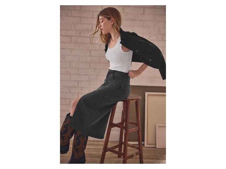 Vrouw in wit topje en zwarte jeansrok zit op een houten kruk.