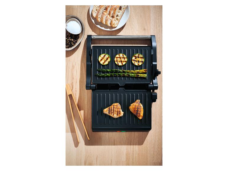 Open grill met gegrilde kip, courgette, asperges en brood op een houten tafel.