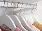 Witte kledinghangers met roze en bruine kleding in een kast.