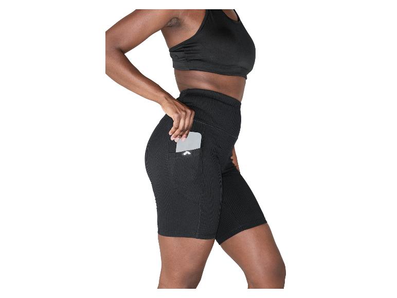 Vrouw in zwarte geribbelde sportbeha en fietsbroek met telefoon in zijzak.