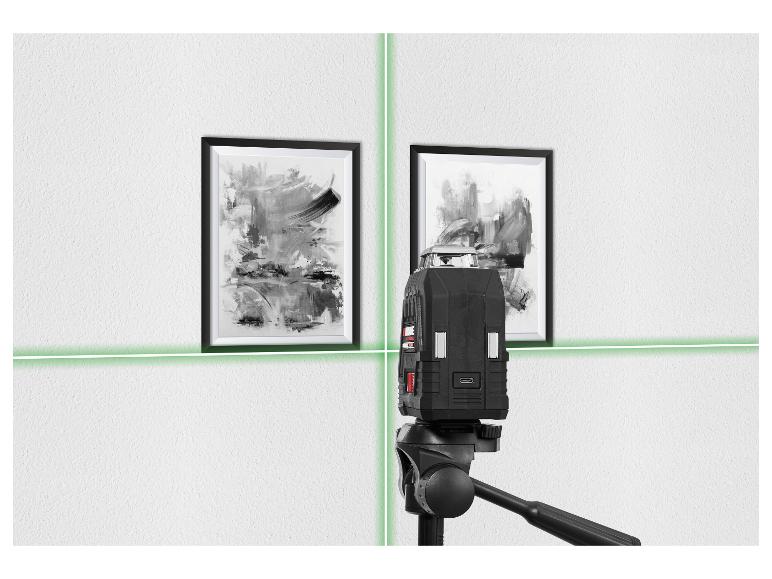 Een laserwaterpas projecteert groene lijnen op een witte muur met twee ingelijste abstracte schilderijen.