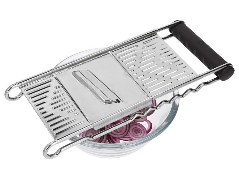 Metalen keukenmandoline met zwarte handvatten boven een glazen kom met gesneden rode ui.