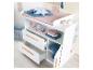 Witte commode met lades en planken, versierd met babyaccessoires en speelgoed.