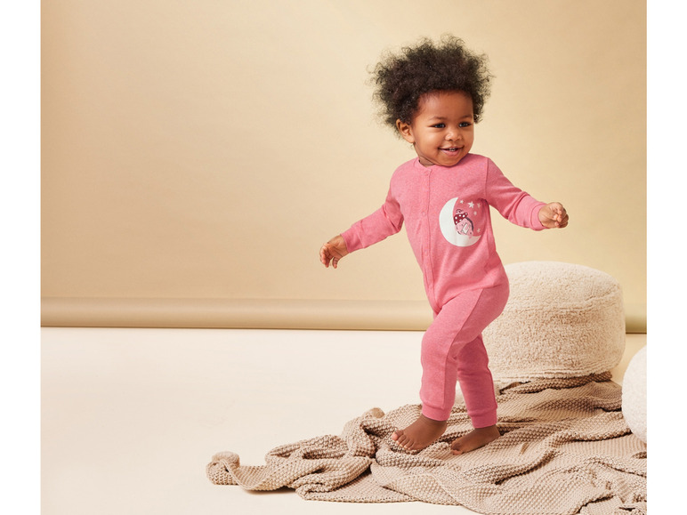 Een baby in een roze slaappak met maan- en stermotief.