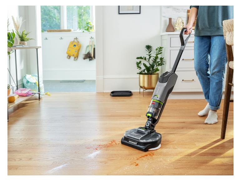 Persoon reinigt houten vloer met een Bissell SpinWave Vac die gemorste vloeistoffen opruimt.