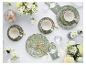 Elegante tafelsetting met groene bloemenborden, witte kopjes, gouden bestek en witte bloemen.