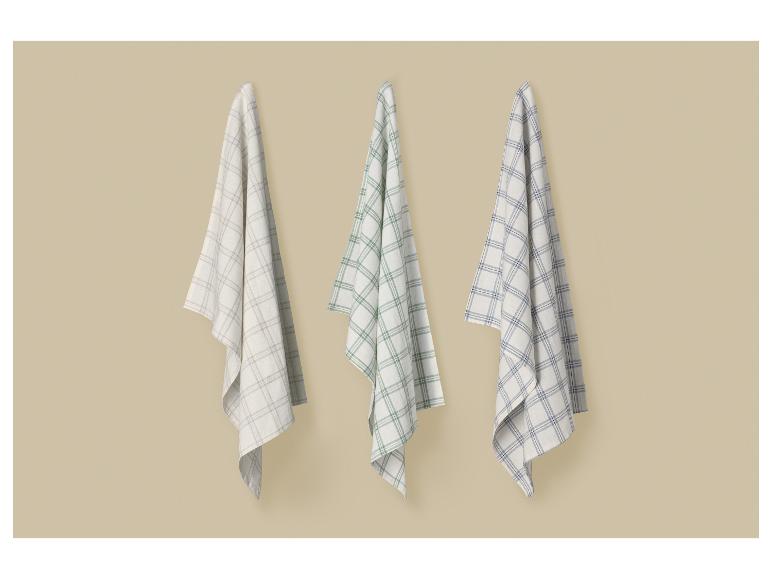 Drie geruite theedoeken in beige, groen en blauw hangen aan een muur.