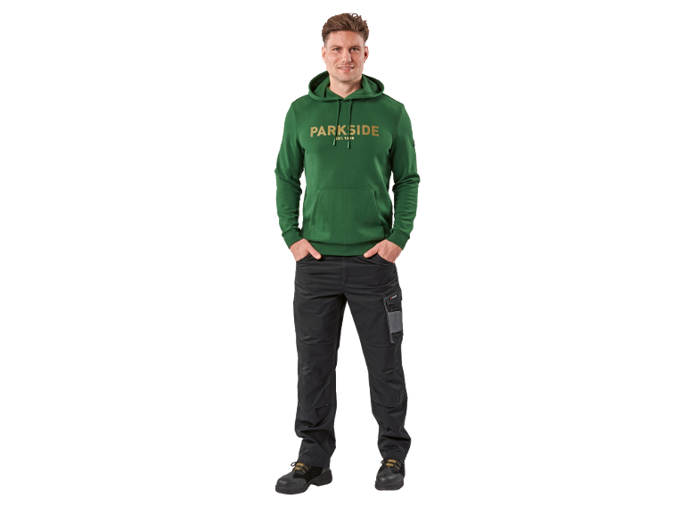Man in groene hoodie met tekst en zwarte werkbroek.