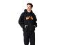 Lachende man in een zwarte hoodie met oranje patroon en zwarte joggingbroek.