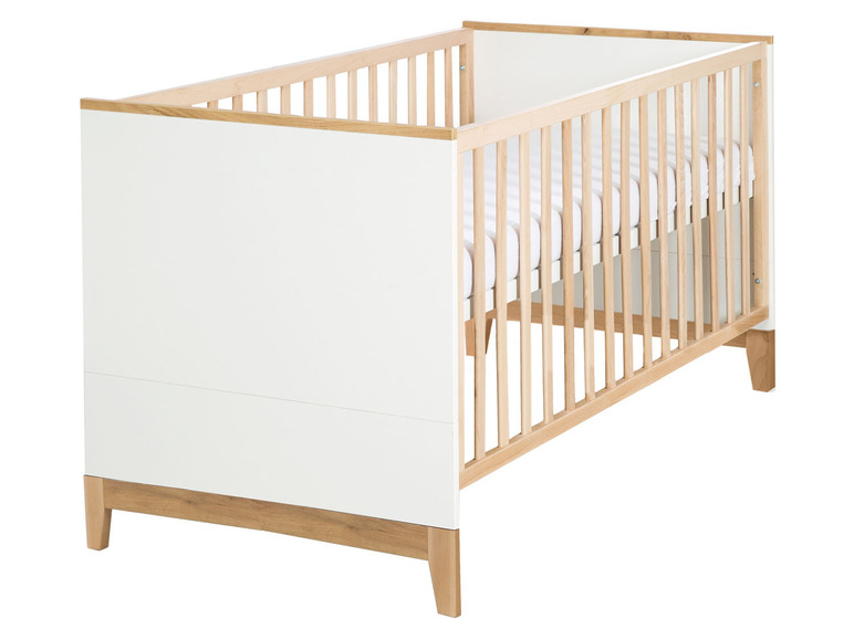 Een wit babybedje met houten spijlen en poten.