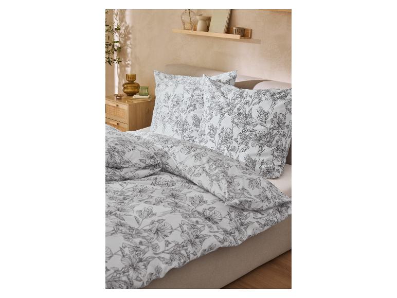 Bed met wit beddengoed met zwarte bloemenprint en een houten nachtkastje.
