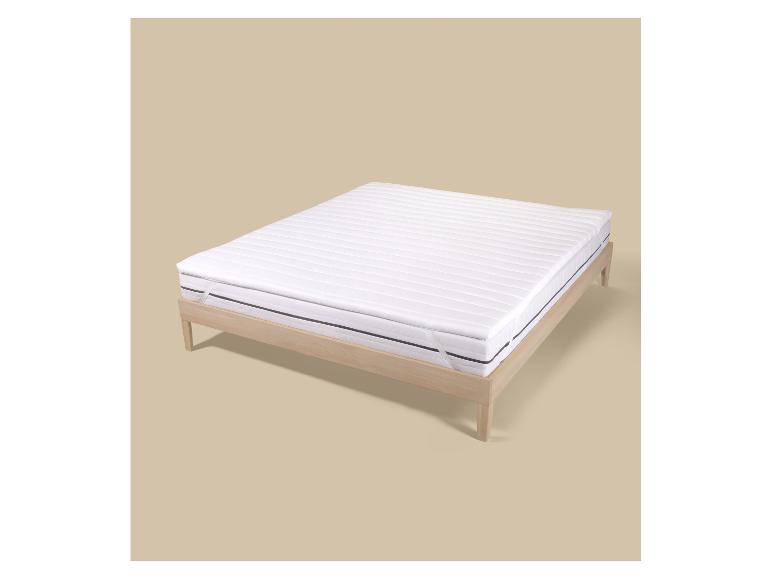 Wit matras met topper in een licht houten bedframe op een beige achtergrond.